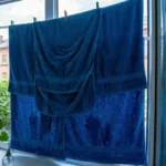 Вологий синій рушник висить перед відкритим вікном для охолодження спальні без кондиціонера