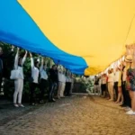 Люди тримають великий прапор України над бруківкою вулиці під час демонстрації