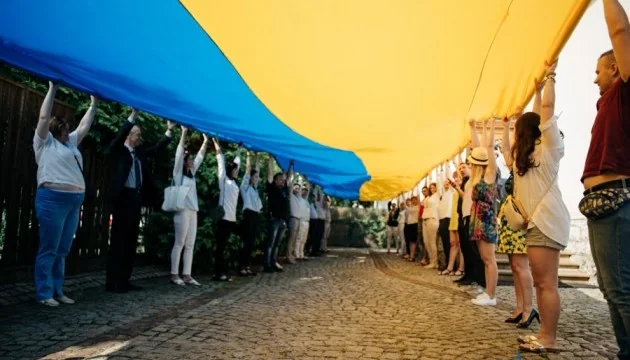 Люди тримають великий прапор України над бруківкою вулиці під час демонстрації