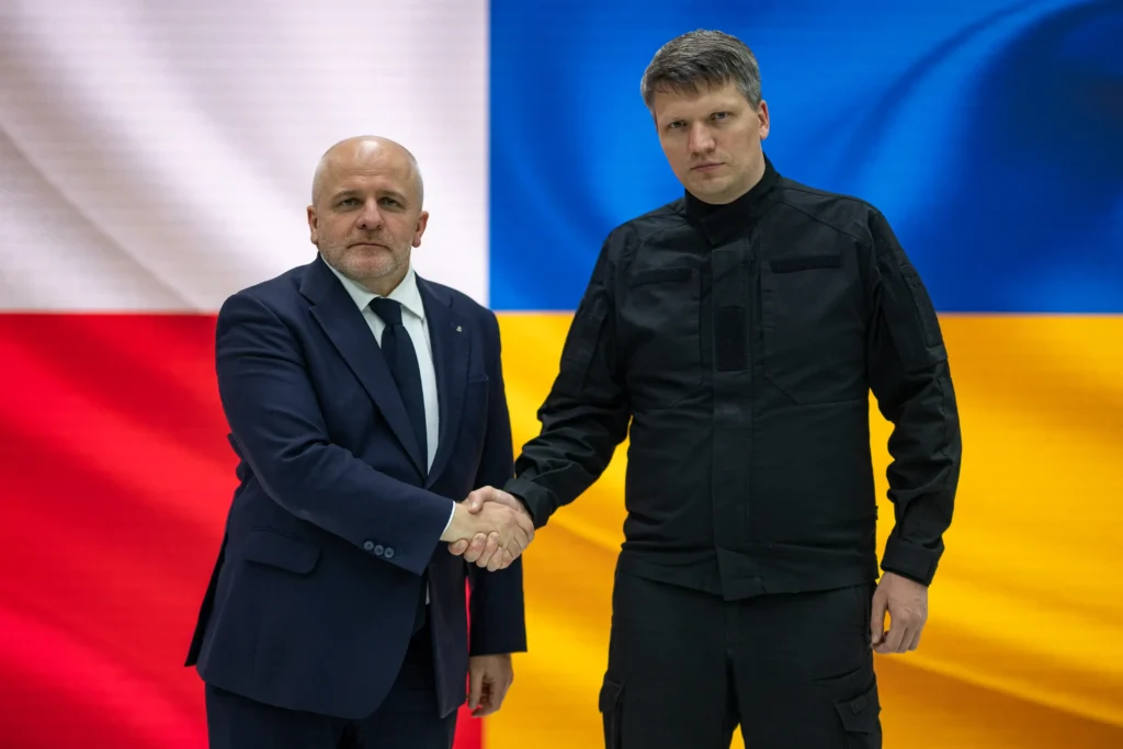 Польский и украинский чиновники жмут руки на фоне флагов Польши и Украины