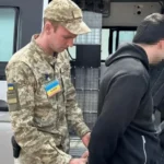Військовослужбовець ТЦК у камуфляжі затримує чоловіка біля мікроавтобуса