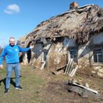 Чоловік біля занедбаної хати-мазанки зі старим соломяним дахом