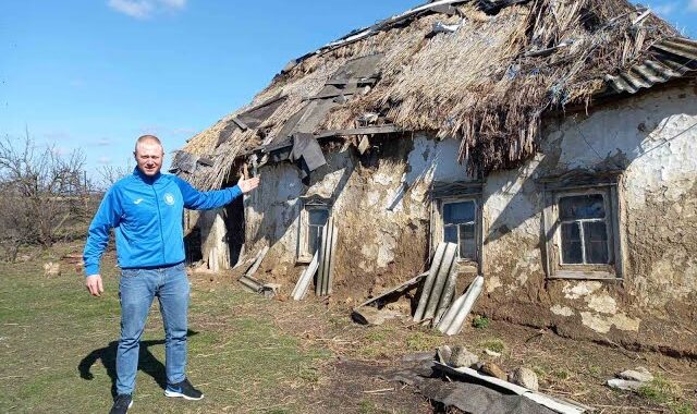Чоловік біля занедбаної хати-мазанки зі старим соломяним дахом