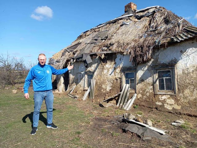 Чоловік біля занедбаної хати-мазанки зі старим соломяним дахом