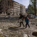 Военный сопровождает женщину среди руин разрушенной Константиновки