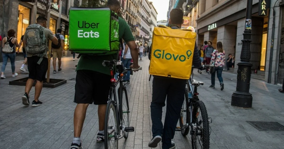 Курьеры Uber Eats и Glovo с рюкзаками на улице после сделки Uber и Delivery Hero