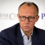 Фрідріх Мерц у синьому костюмі з окулярами на фоні Presse Club München