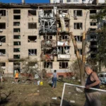 Зруйнована багатоповерхівка після обстрілу, люди серед уламків на подвір’ї