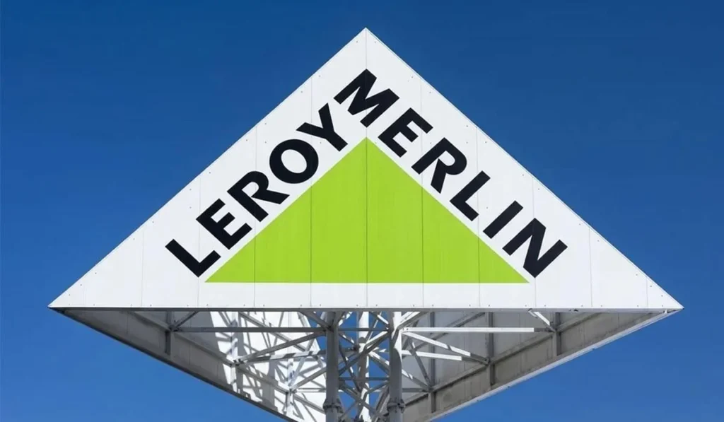 Біла трикутна вивіска Leroy Merlin із зеленим трикутником на тлі синього неба