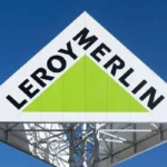 Біла трикутна вивіска Leroy Merlin із зеленим трикутником на тлі синього неба