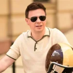 Дмитро Комаров в окулярах тримає шолом біля скутера