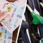 Рука тримає банкноти 1000 гривень поруч із заправними пістолетами