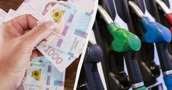 Рука тримає банкноти 1000 гривень поруч із заправними пістолетами