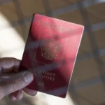 Рука тримає червоний паспорт Російської Федерації на тлі віконної сітки
