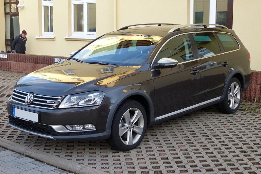 Темно-сірий універсал Volkswagen Passat Alltrack припаркований на бруківці біля жовтого будинку