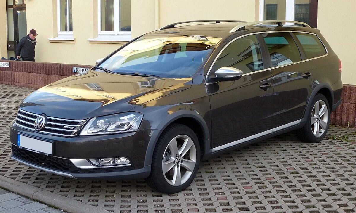 Темно-сірий універсал Volkswagen Passat Alltrack припаркований на бруківці біля жовтого будинку