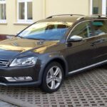 Темно-сірий універсал Volkswagen Passat Alltrack припаркований на бруківці біля жовтого будинку